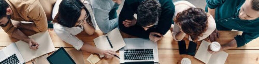 Top view of young modern people in smart casual wear using modern technologies while working in the creative office